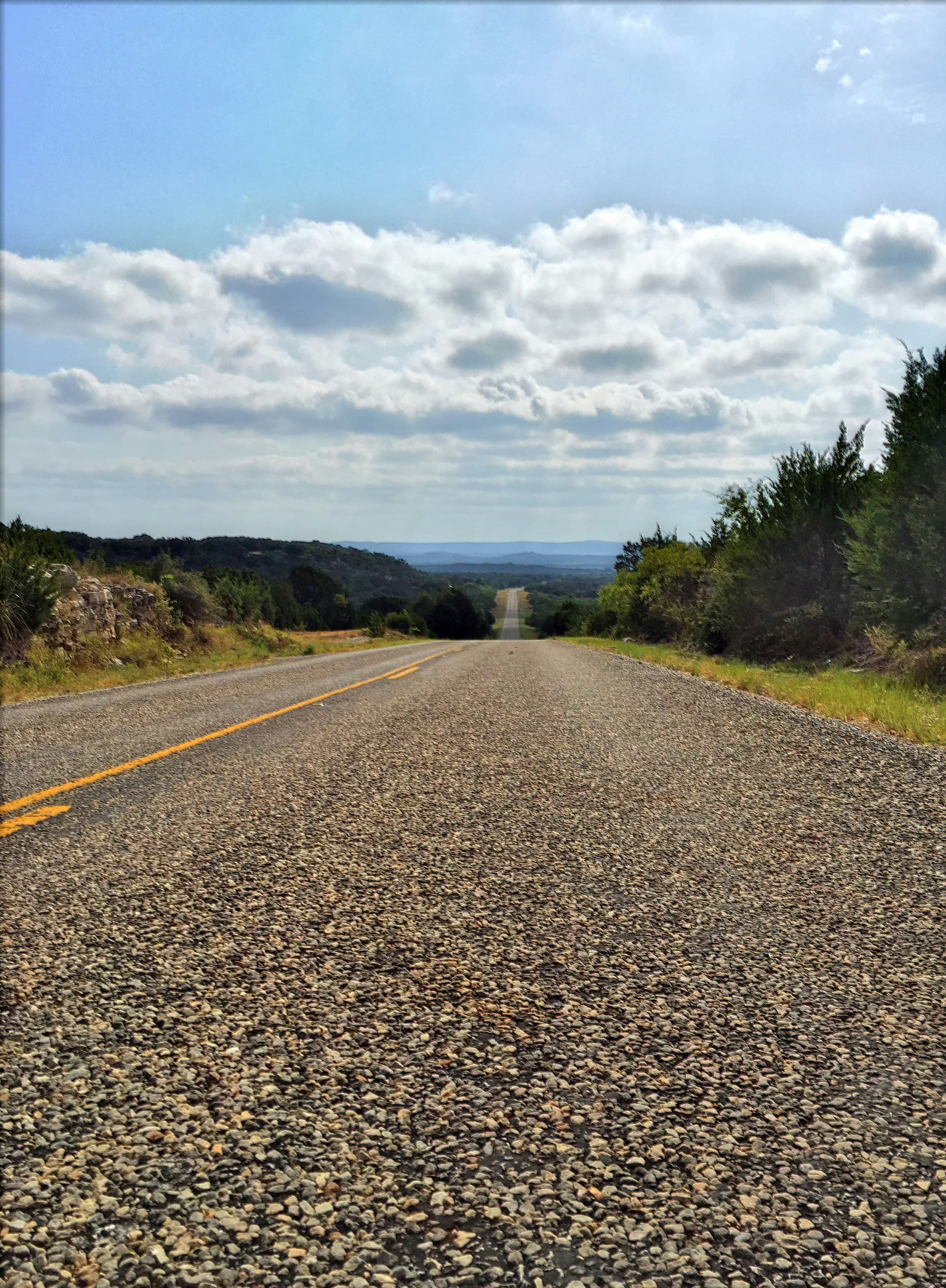 A quiet two-lane road stretching toward the Texas hill country horizon