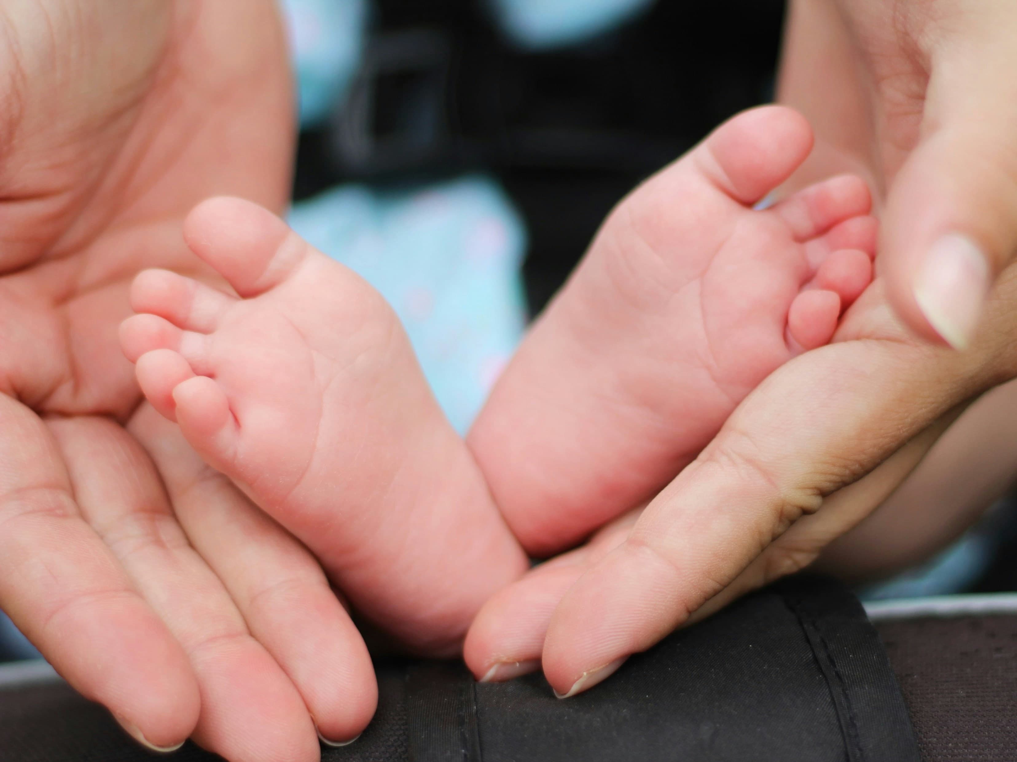 A grandparent's and parent's hands gently cradling a baby's feet