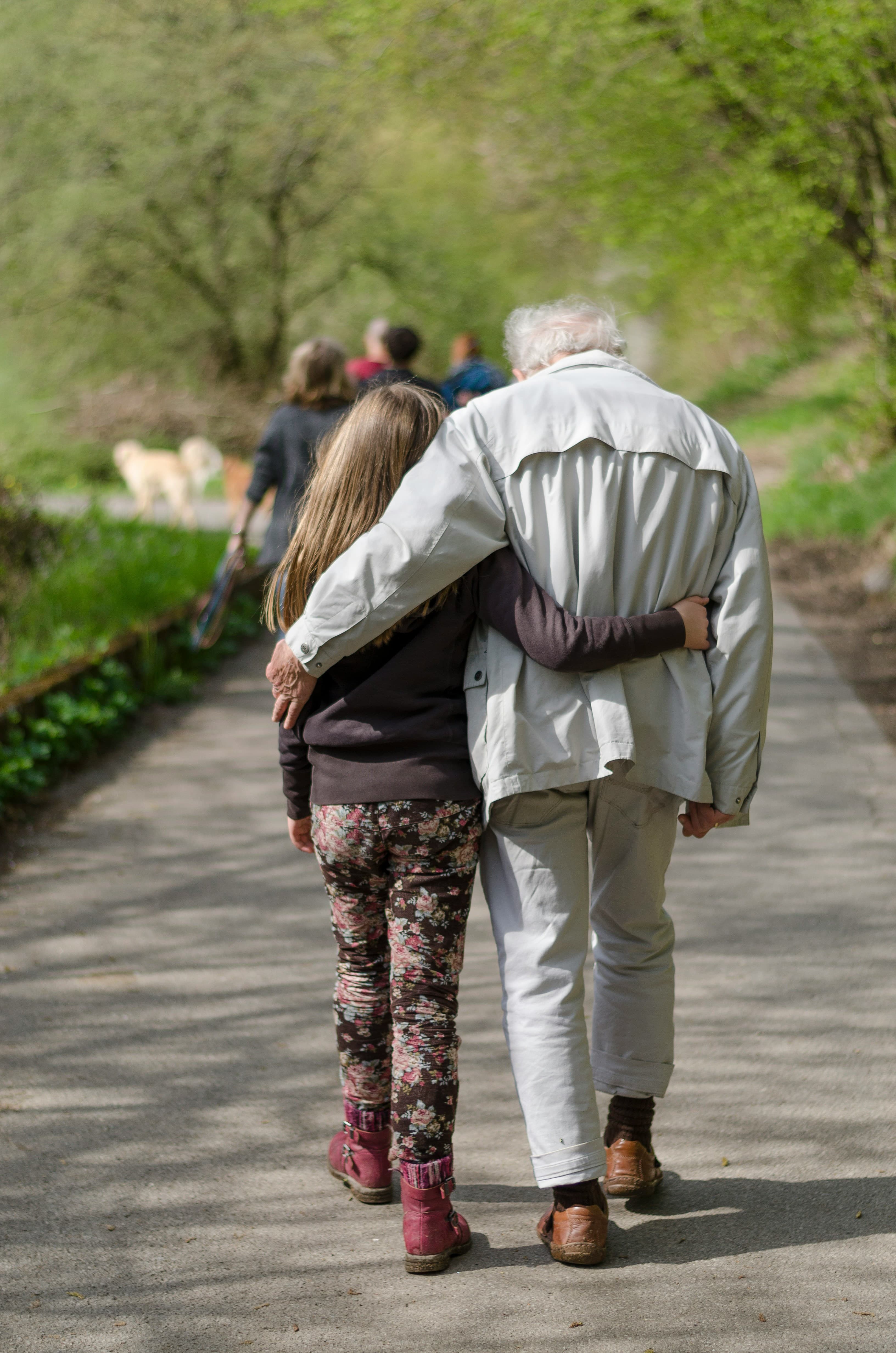 A grandfather and granddaughter walking arm in arm with family following behind